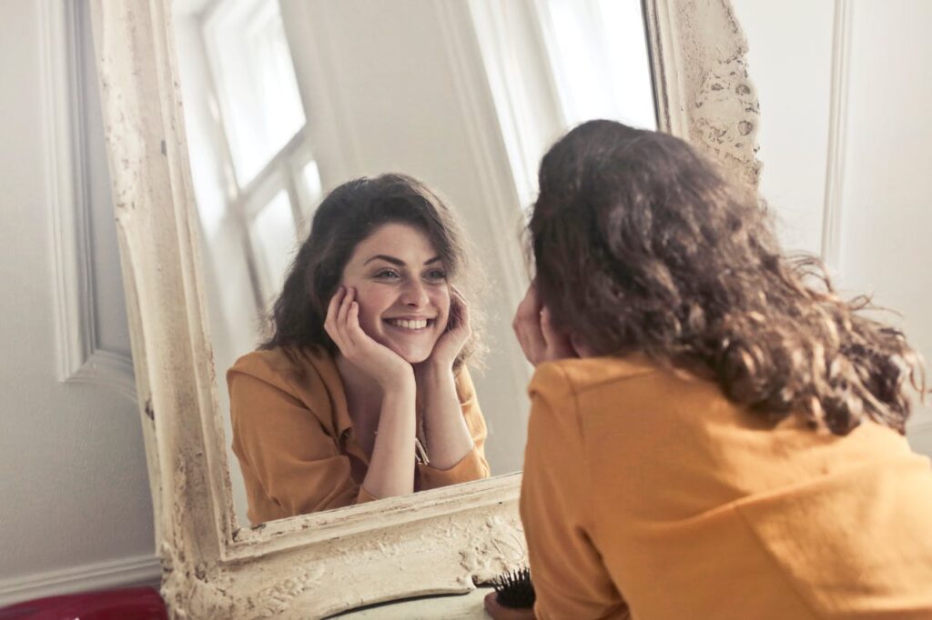 pexels-photo-774866 A cheerful woman smiles at her reflection in a vintage-style mirror, exuding positivity and warmth.